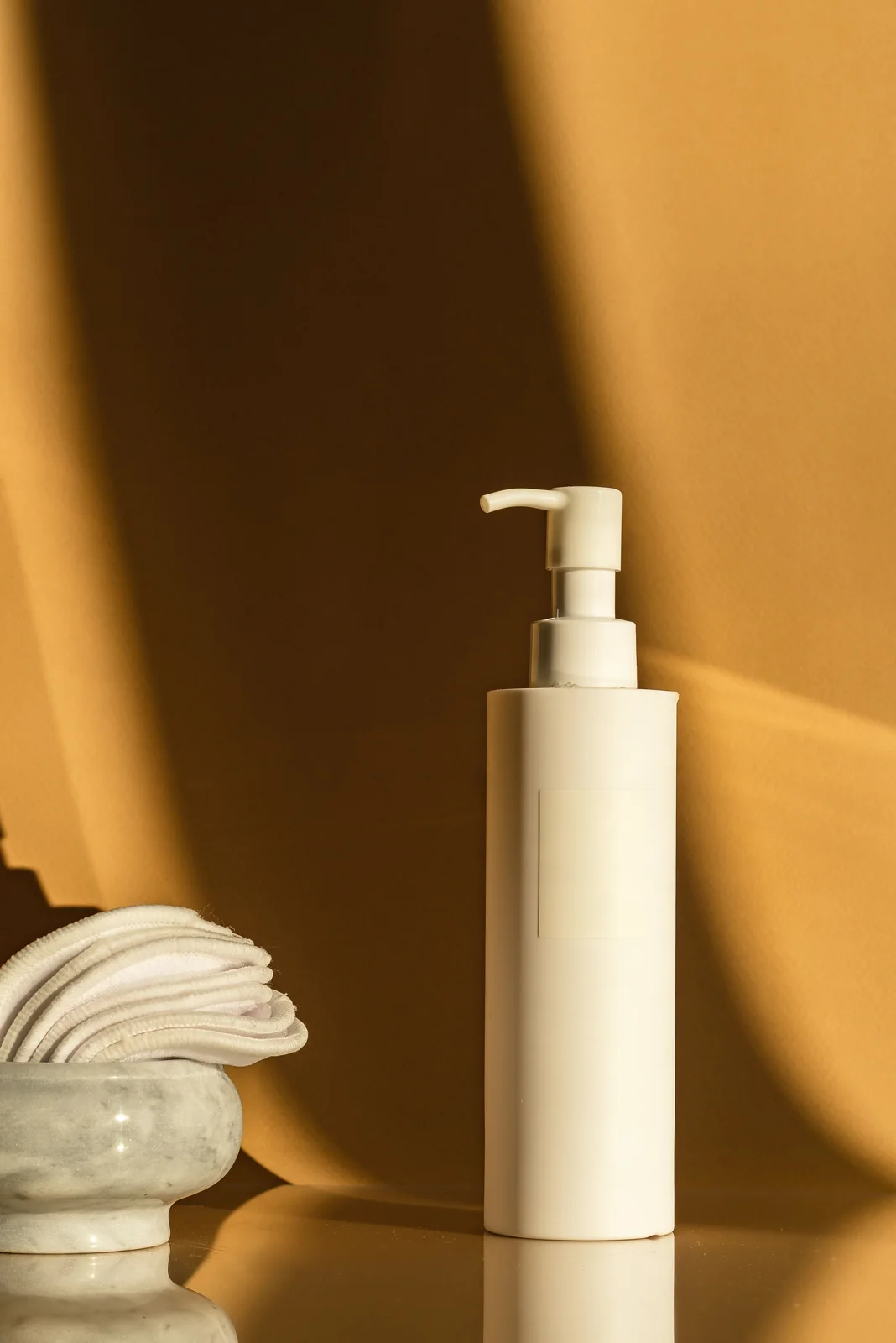 An unlabelled white pump bottle and cotton pads in warm light